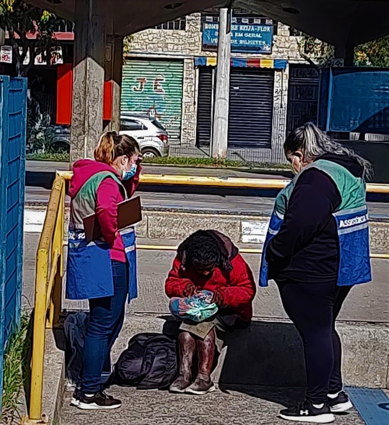 Duas pessoas da assistência Social ajudando um morador de rua, dando orientações e distribuindo cobertor.